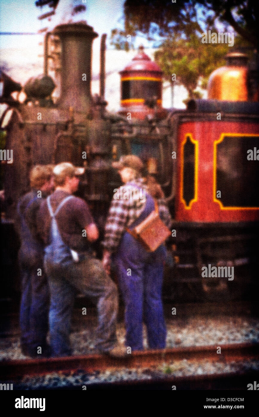 A vintage old style photo of a group of engine drivers and railway workers standing beside an old working steam train. Stock Photo