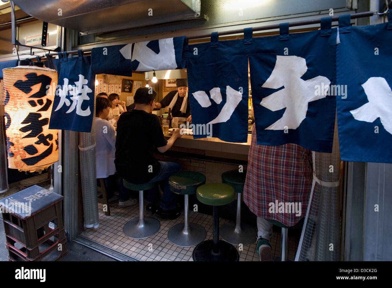 Patrons behind noren curtain enjoy good food and friendship at counter eatery in Omoide Yokocho, Memory Lane, Shinjuku, Tokyo Stock Photo