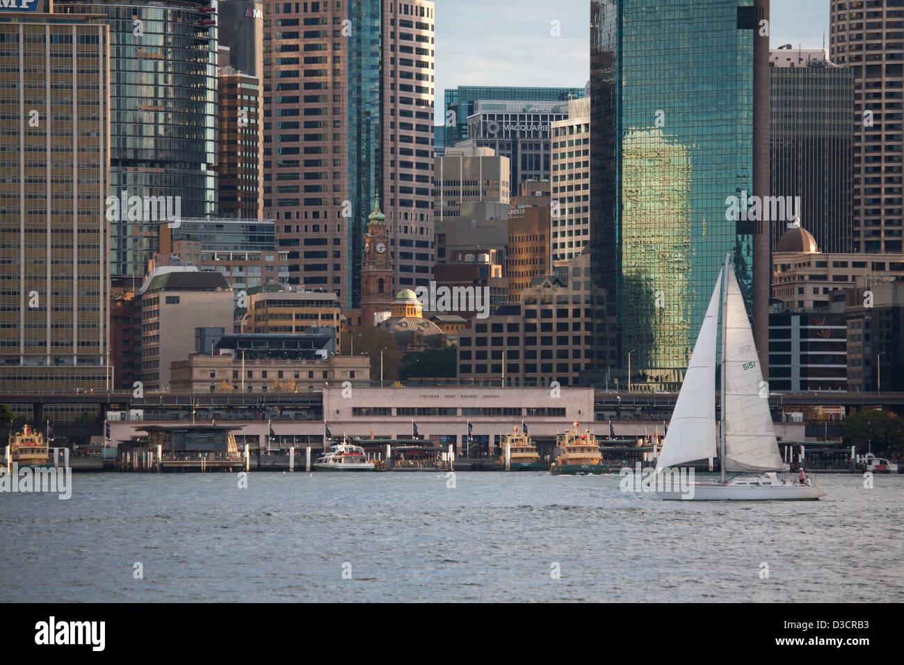 Solo yacht sailing in front of the entrance to Circular Quay Ferry Terminal and Railway Station in the late afternoon light Stock Photo