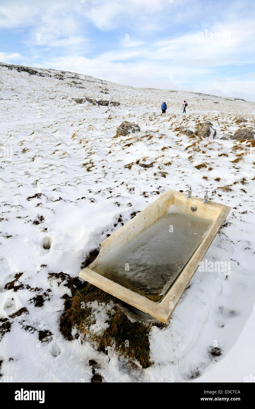 Disused cast iron bath full of frozen water and being used as a drinking trough for sheep on the moors above Malham cove. Stock Photo