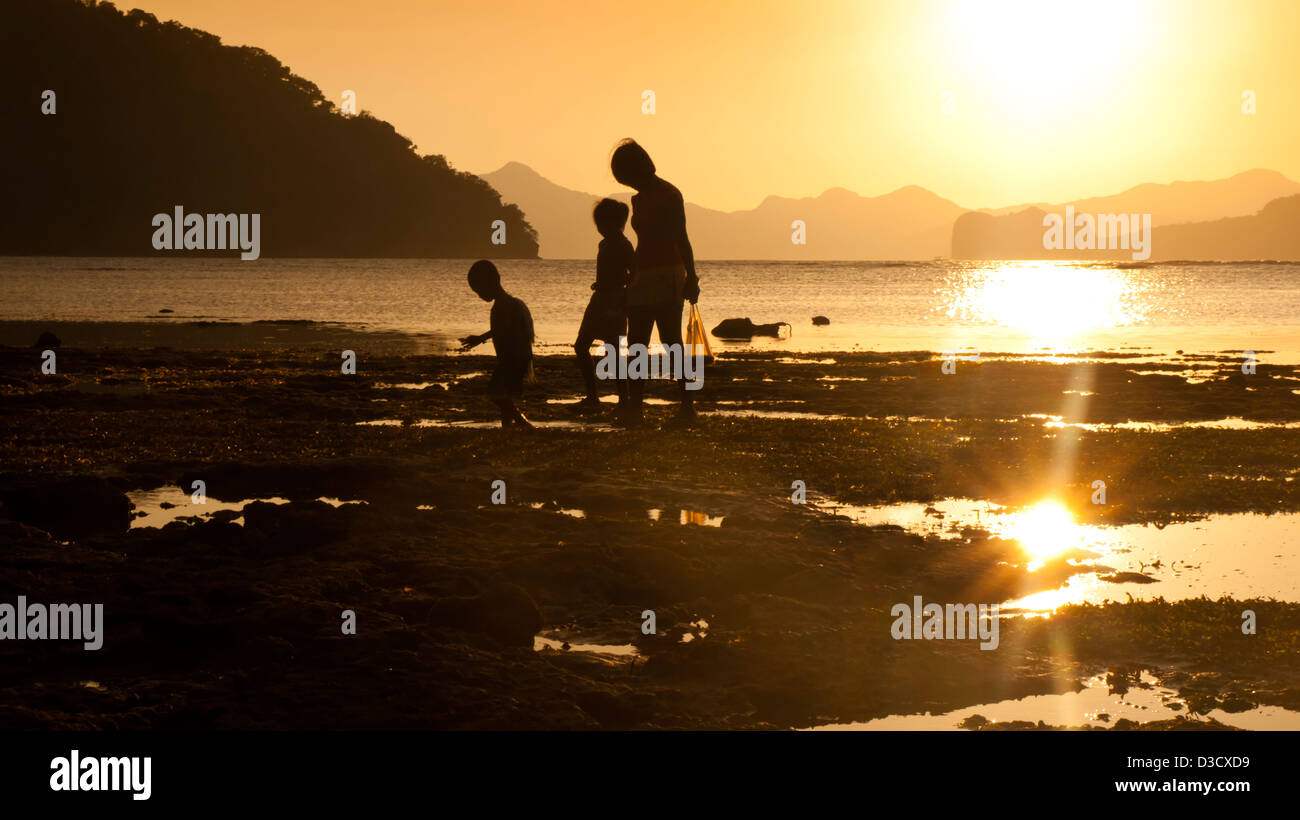 Mother and children silhouette at sea sunset, they are walking along the beach. Stock Photo