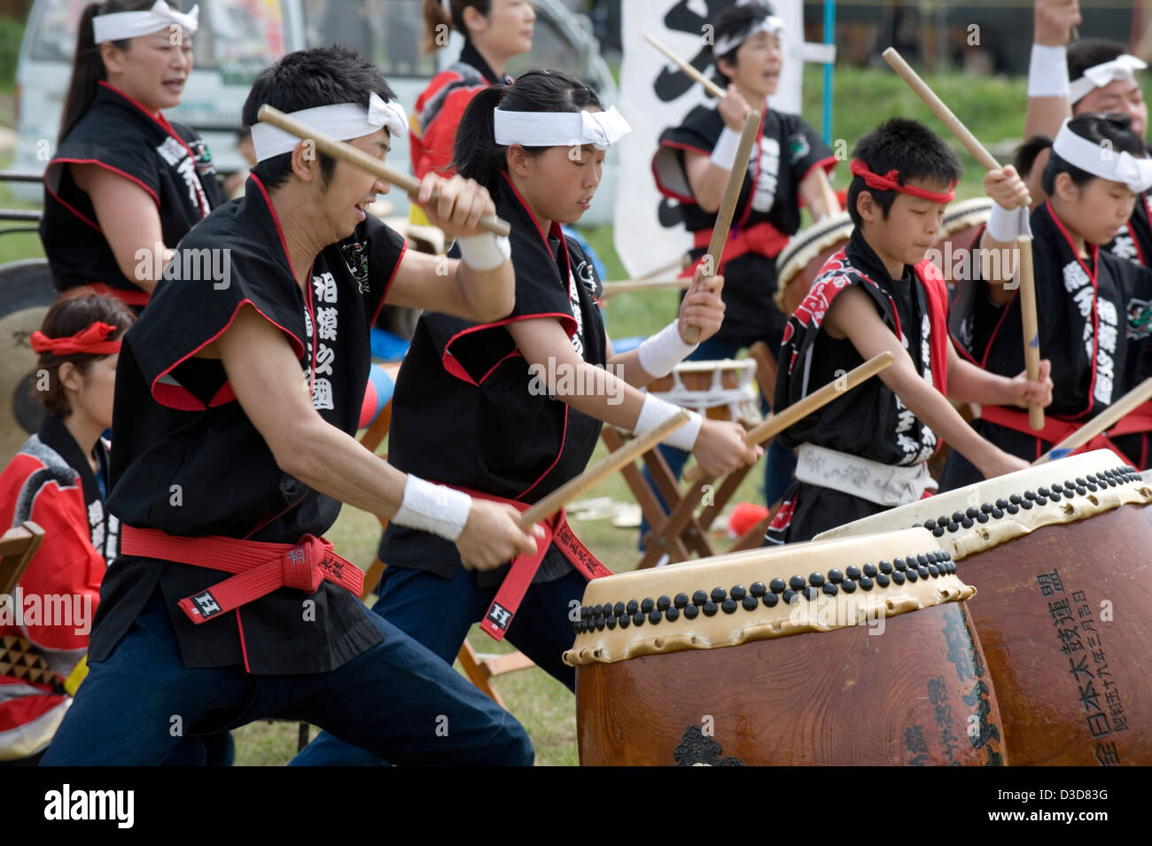 A team of energetic drummers young and old beat a musical rhythm on odaiko Japanese drums with wooden mallets at a festival. Stock Photo