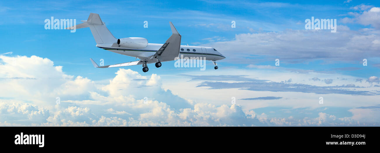 Private jet is maneuvering for landing in a cloudy sky. Panoramic composition. Stock Photo
