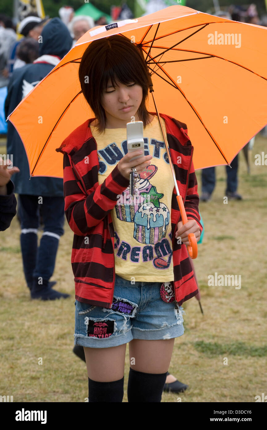 A casual but fashionable Japanese teenage girl checks her mobile phone for text messages. Stock Photo