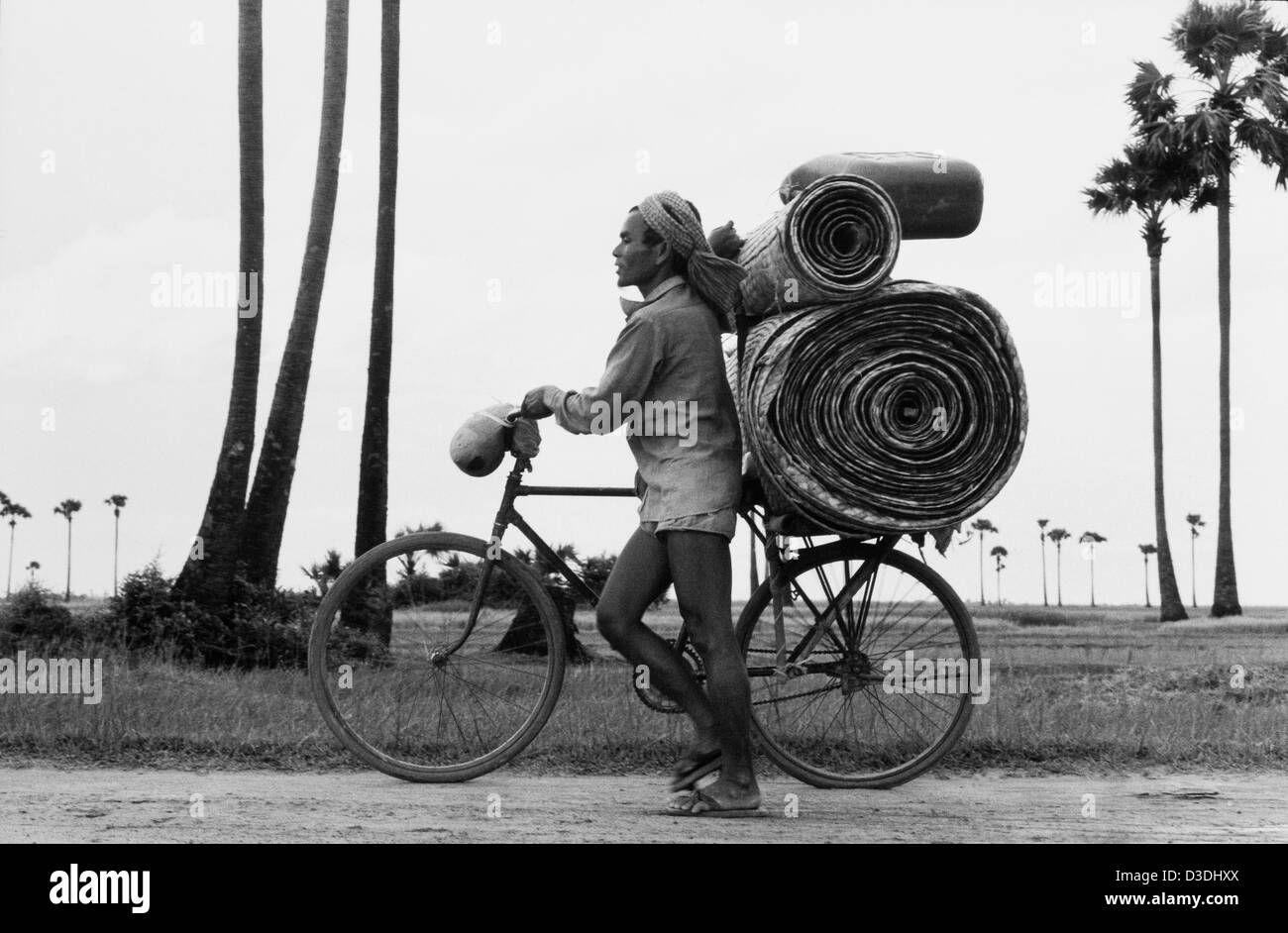 Prey Veng province, Cambodia: Carrying woven mats to market along the village road, with sugar palms in the background. Stock Photo