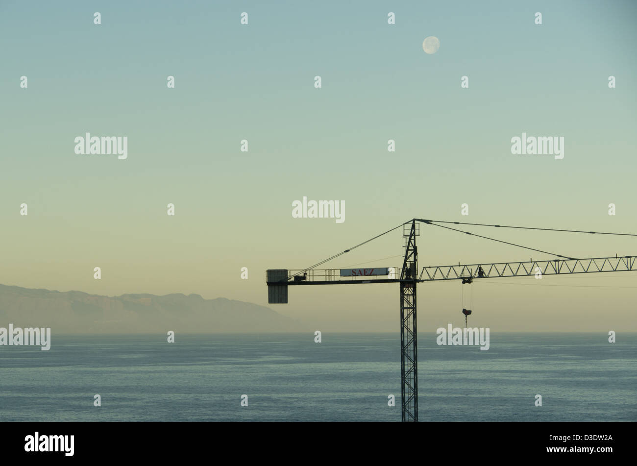Construction crane and moon, with strait between La Gomera and Tenerife in the background Stock Photo
