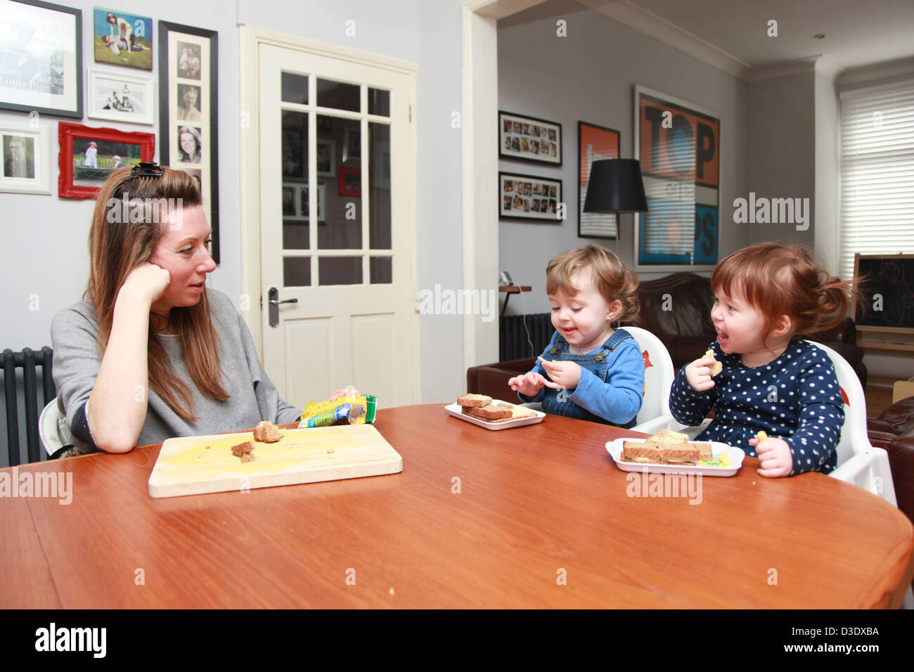 Mum feeding year old twin girls at the table. Stock Photo