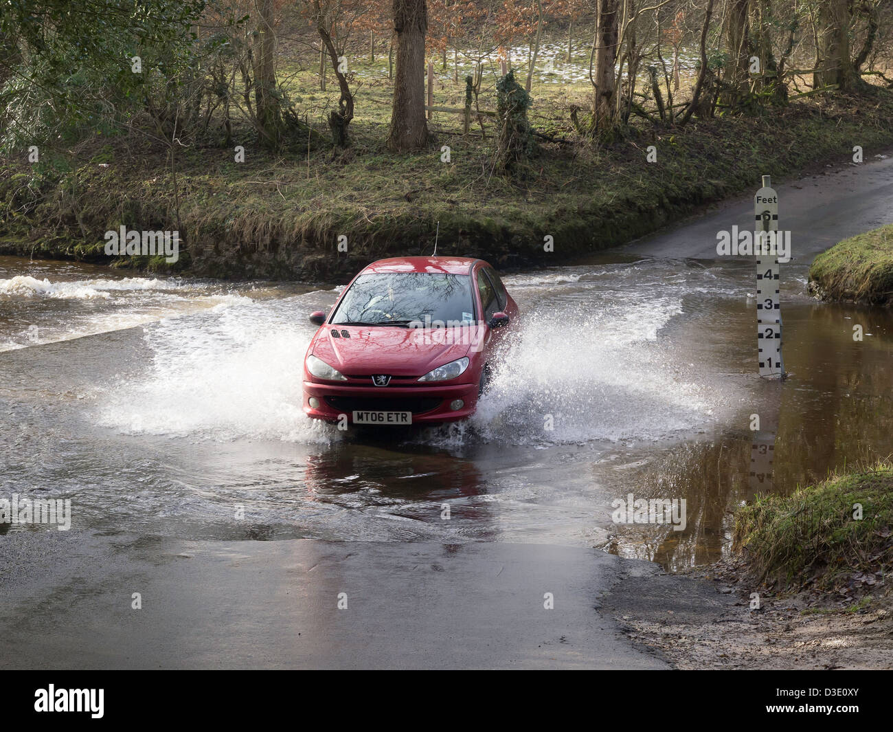 A red Peugeot motor car driven fast crossing a ford over a stream in the North Yorkshire Moors Stock Photo