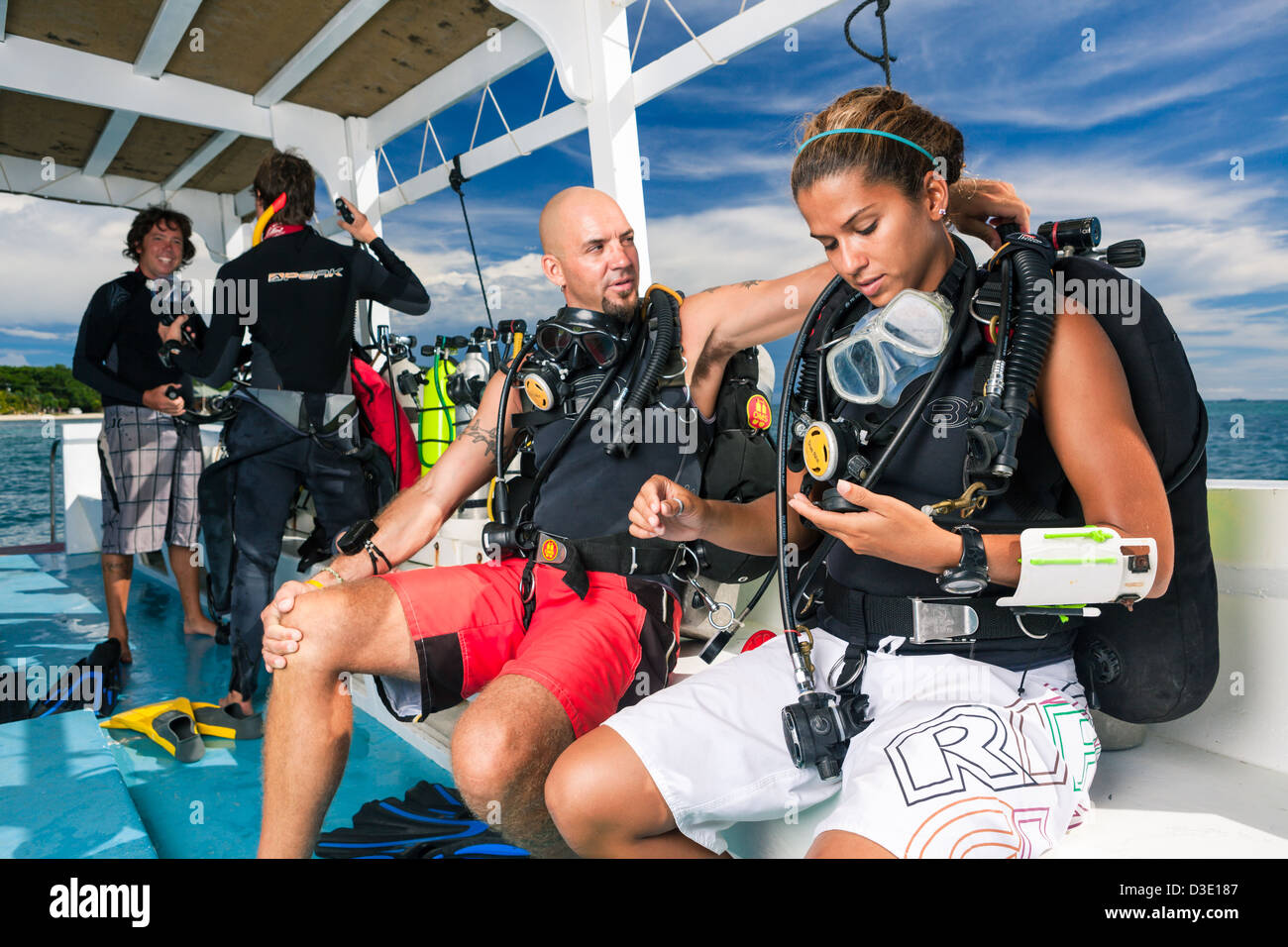 An instructor helps student with diving equipment on boat while preparing for scuba dive. Stock Photo