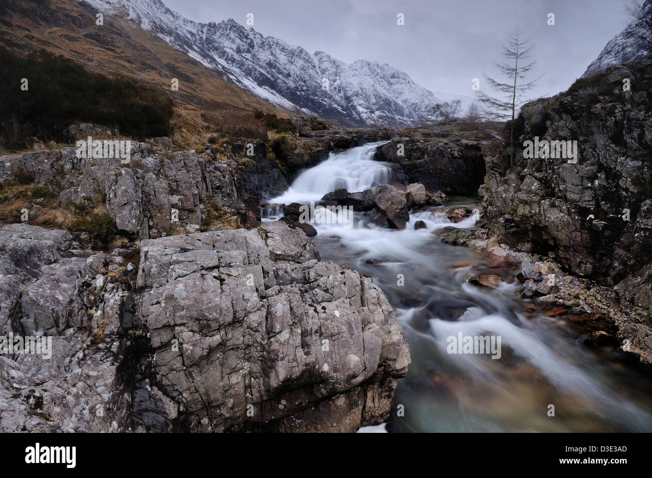 Rocky section of the River Coe, Glencoe, Scotland, with the snow covered Aonach Eagach ridge towering above Stock Photo