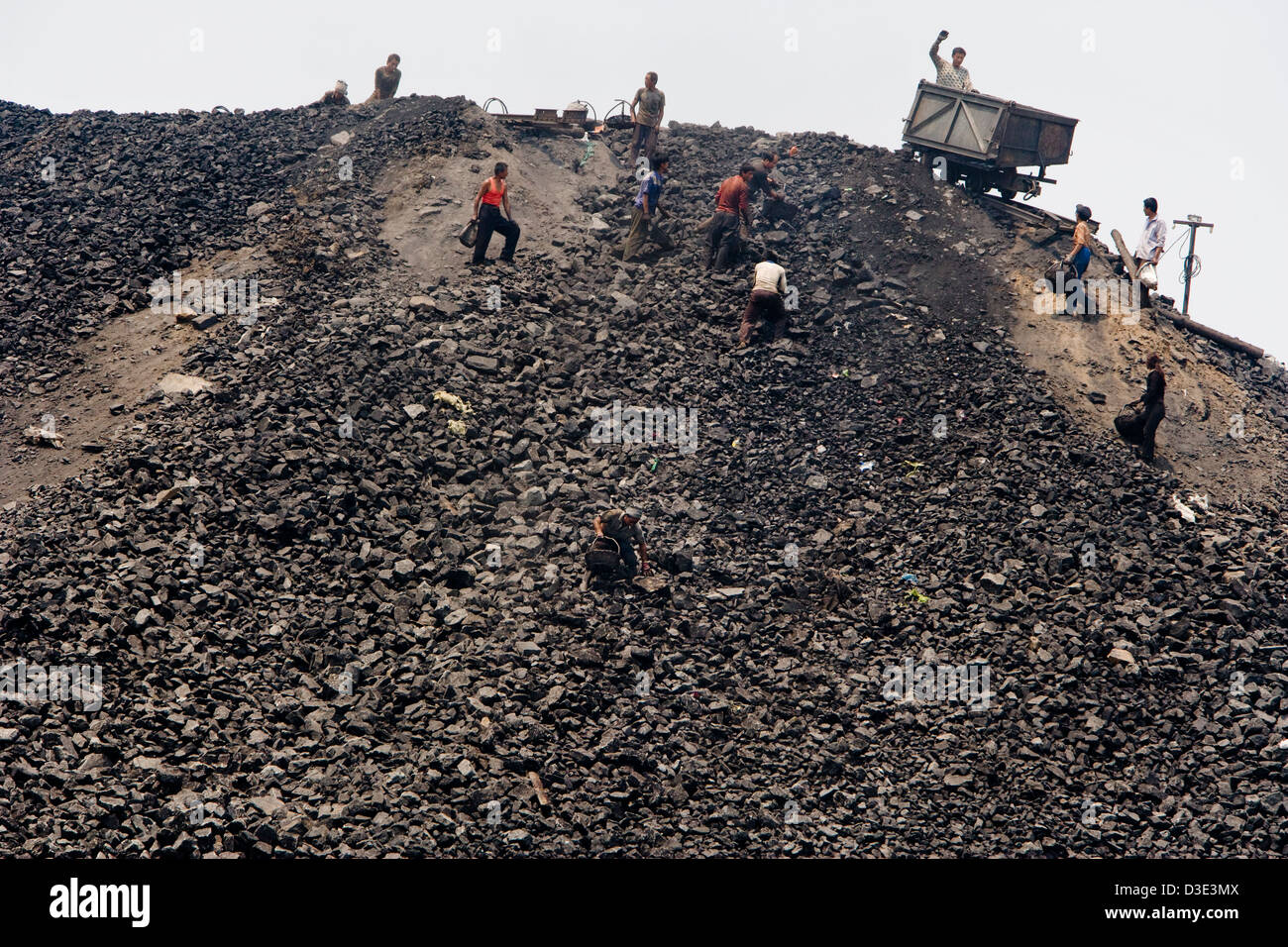 YI TANG, SHANXI PROVINCE, CHINA - AUGUST 2007: Villagers scavenge for scrap coal as a mine rail cart is unloaded onto a slag heap Stock Photo
