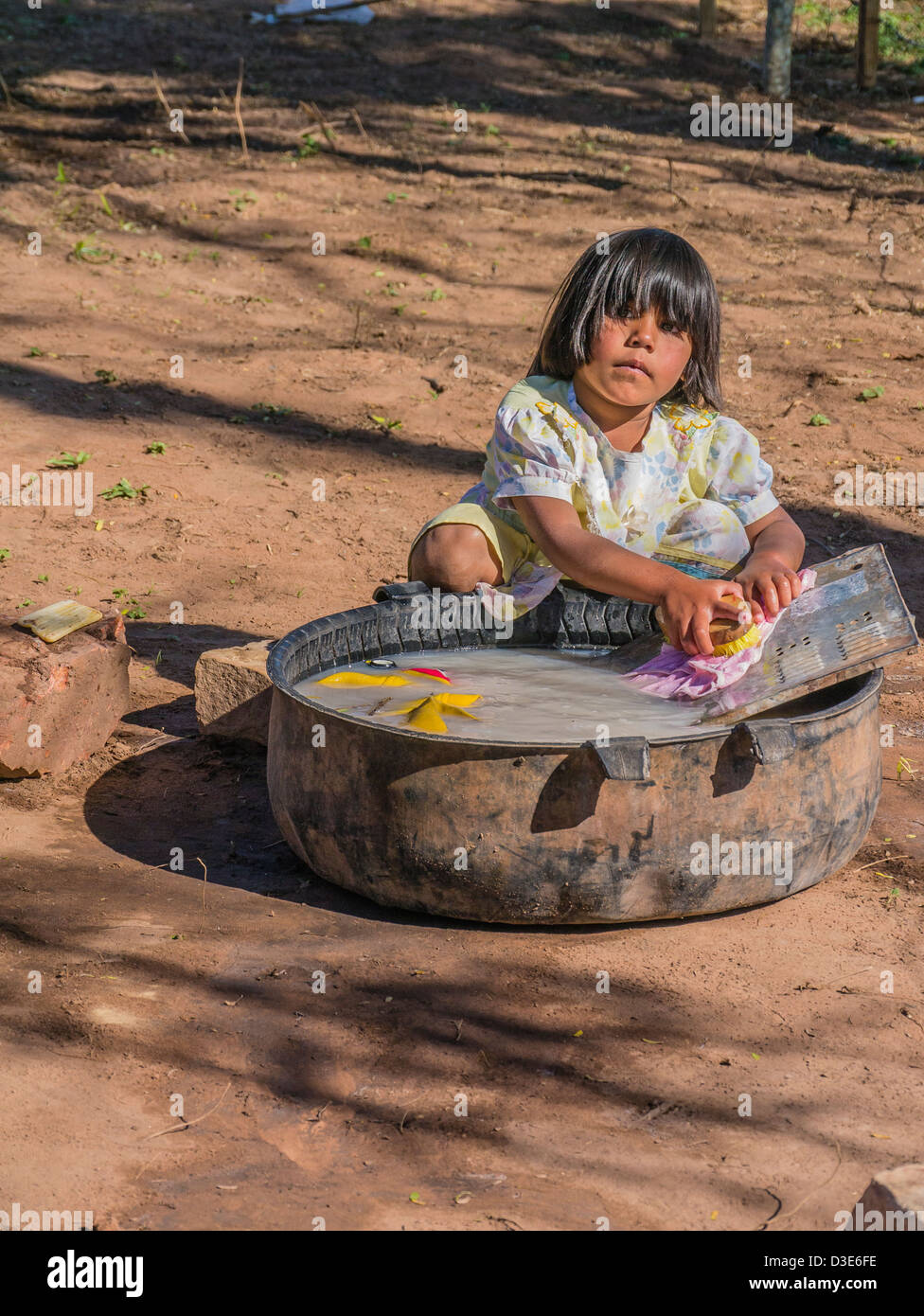 A 4-5 year old Paraguayan girl washes her clothes on the ground outside of her house. Stock Photo