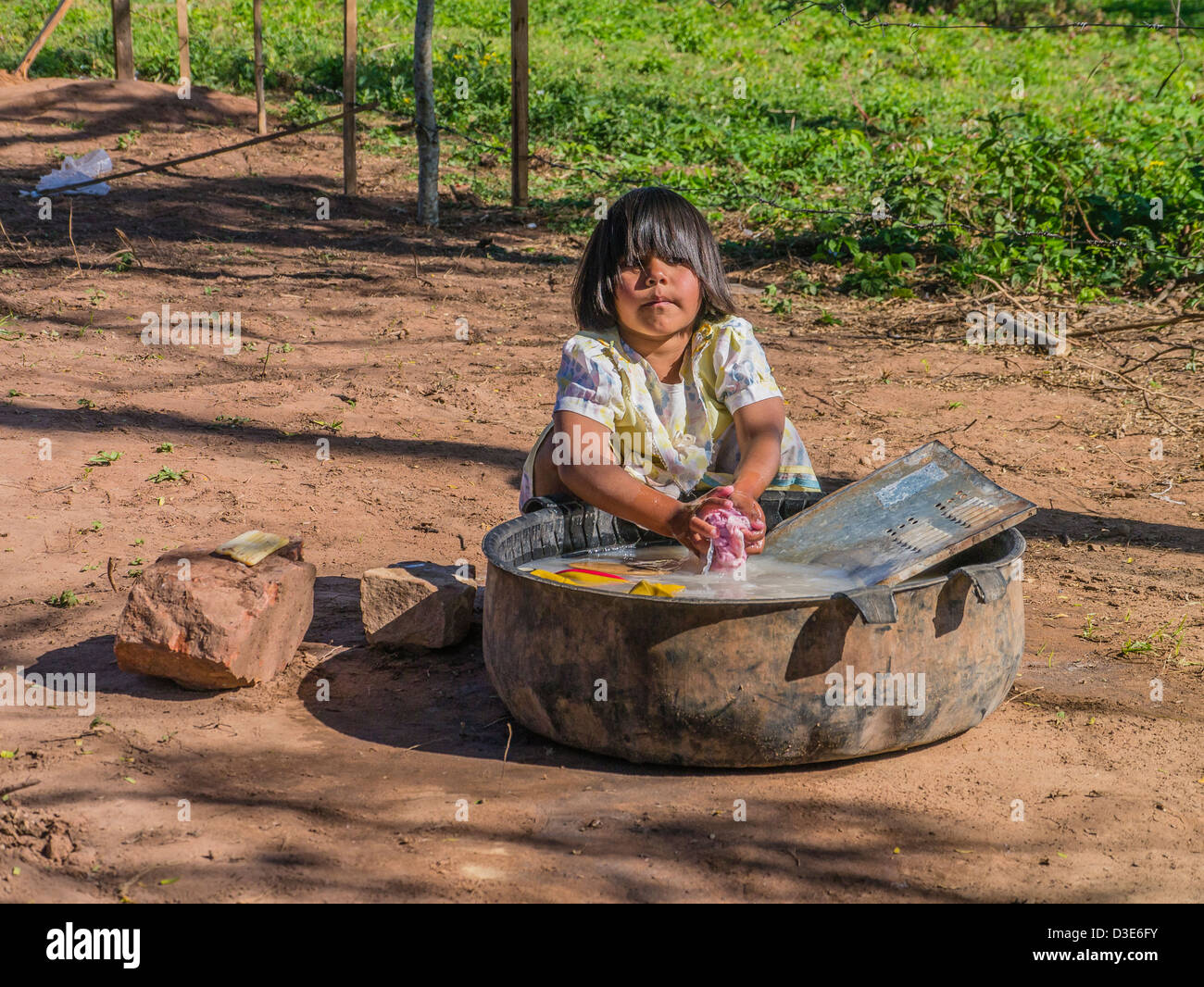 A 4-5 year old Paraguayan girl washes her clothes on the ground outside of her house. Stock Photo