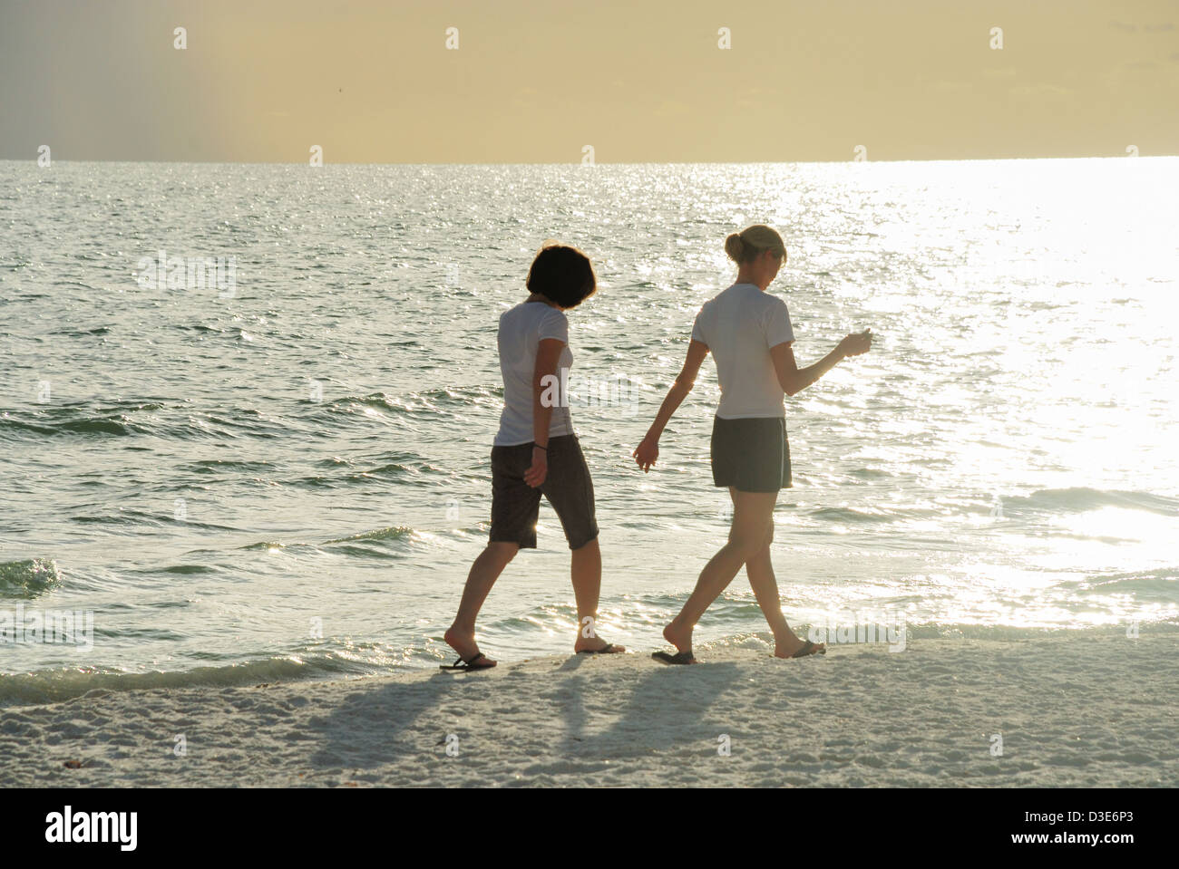 Two young women walk on beach into glow from setting sun Stock Photo ...