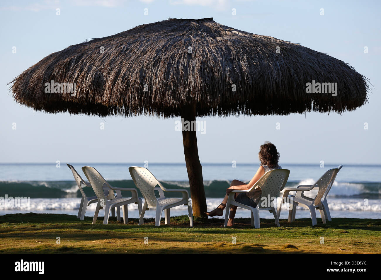 Woman sitting under a large thatched umbrella, Las Lajas, Panama Stock Photo