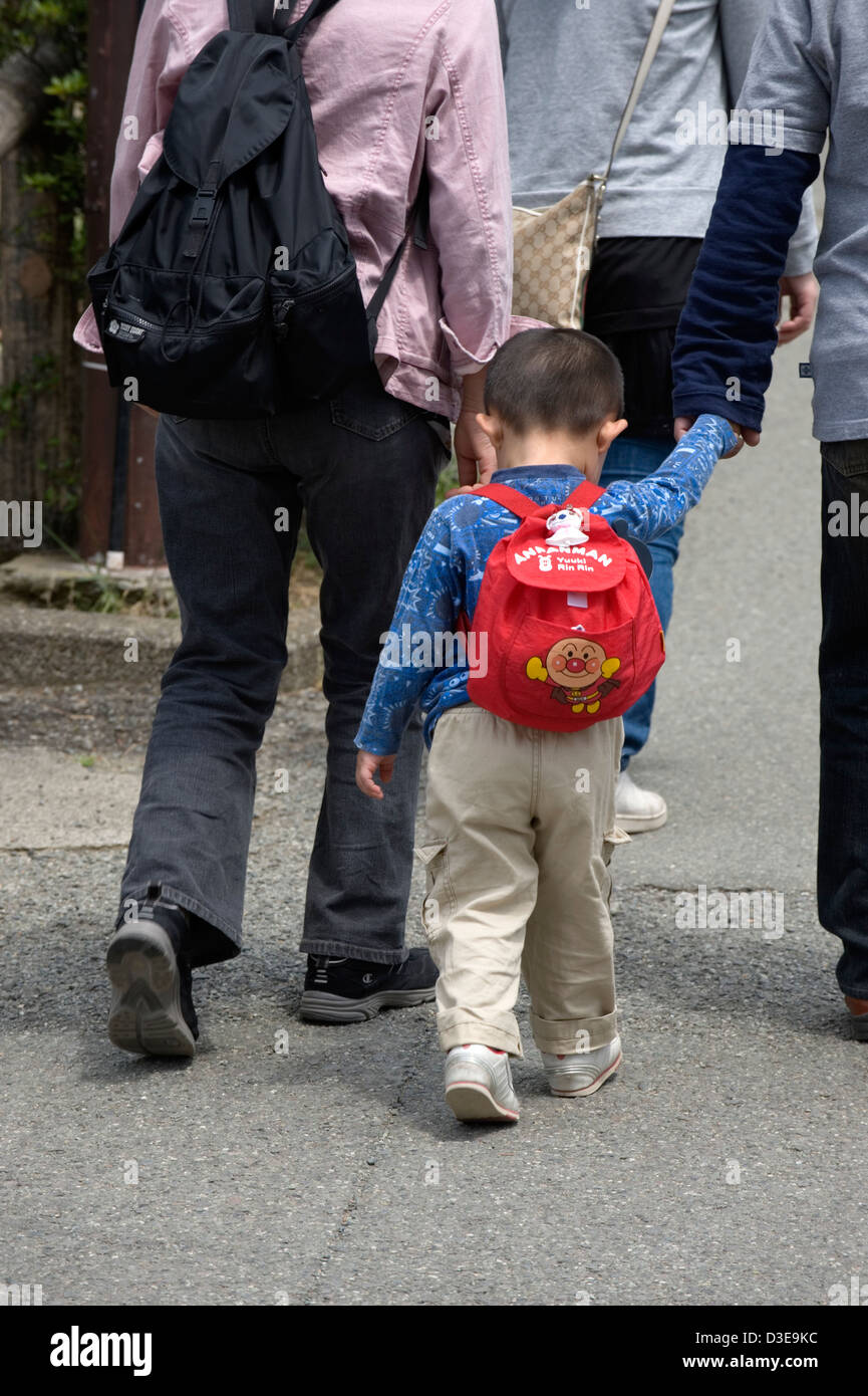 A little Japanese boy wearing an Anpanman backpack walks hand in hand with one of his parents. Stock Photo