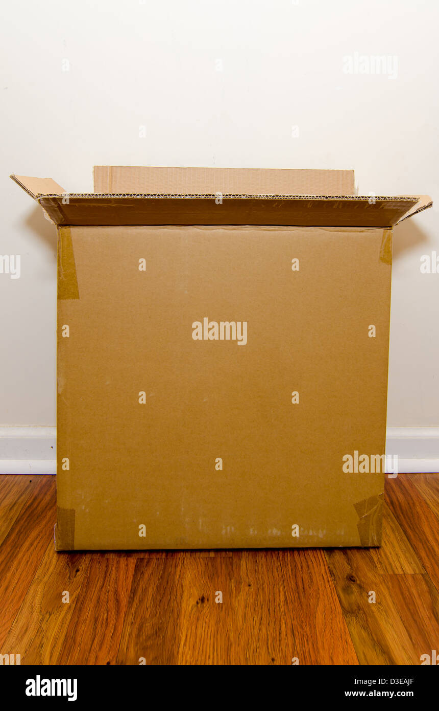 Moving day with empty cardboard box on hardwood floor. Stock Photo