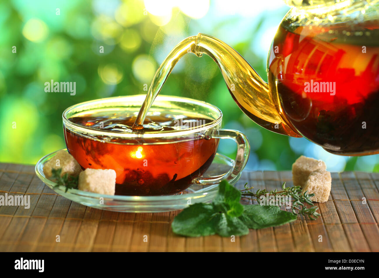 Pouring tea from a teapot into a cup on a blurred background of nature. Stock Photo