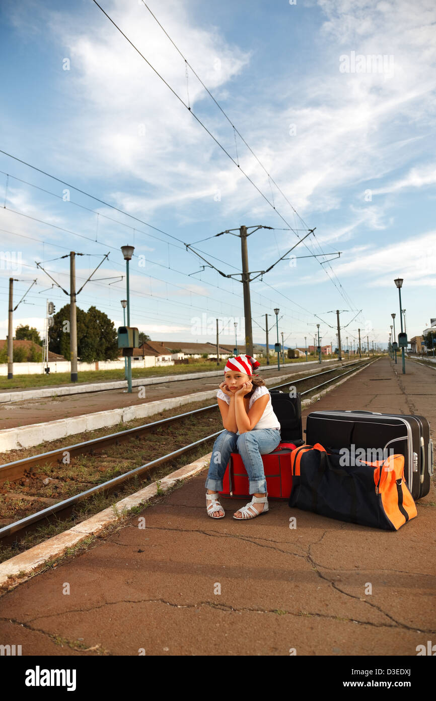 Young girl sitting on luggage and waiting for train in the station Stock Photo