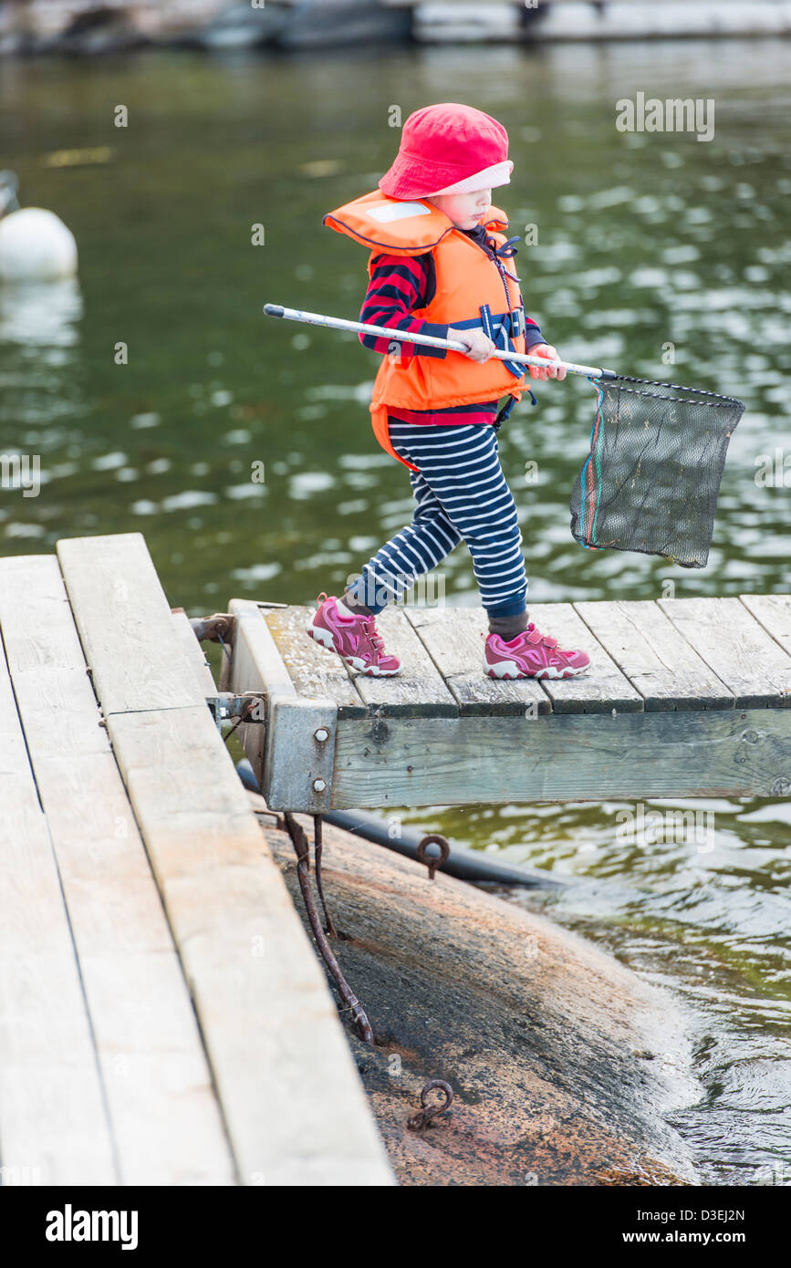 Young child wearing life jacket walking on jetty by the sea holding a fishing net in hand Stock Photo