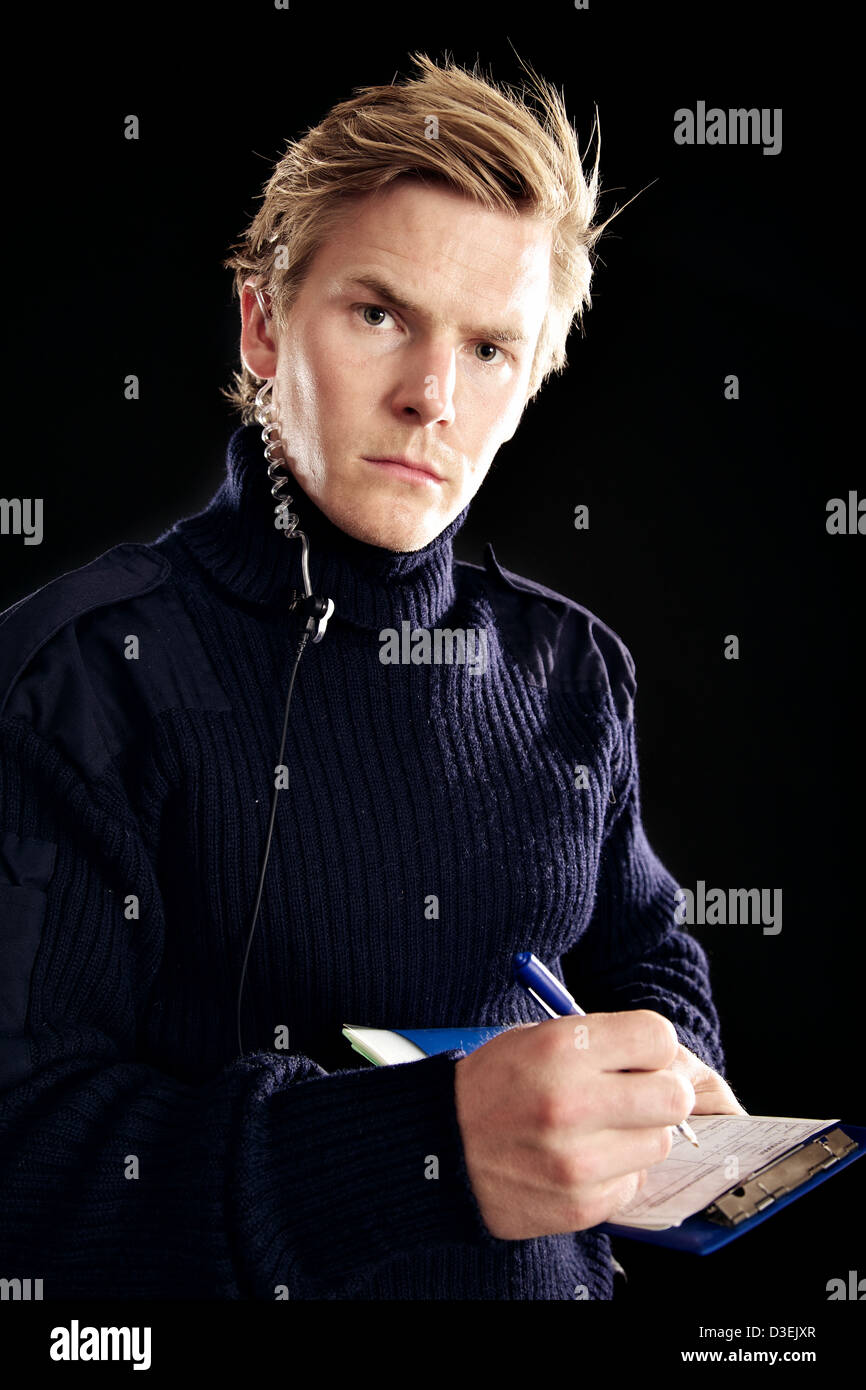 Handsome security officer looking at you while writing something on his note against black background Stock Photo