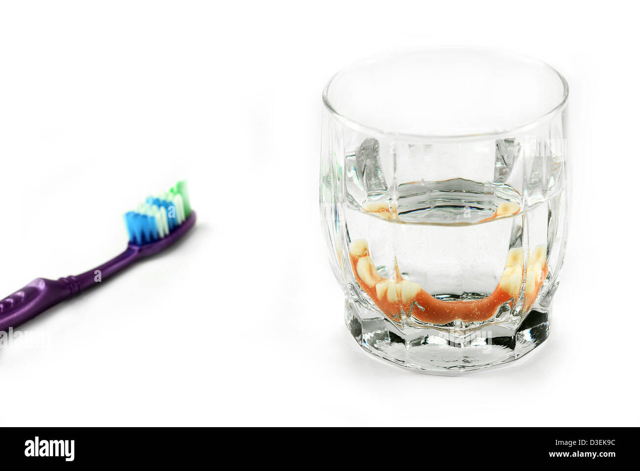 Partial denture inside glass next to toothbrush, isolated on white Stock Photo