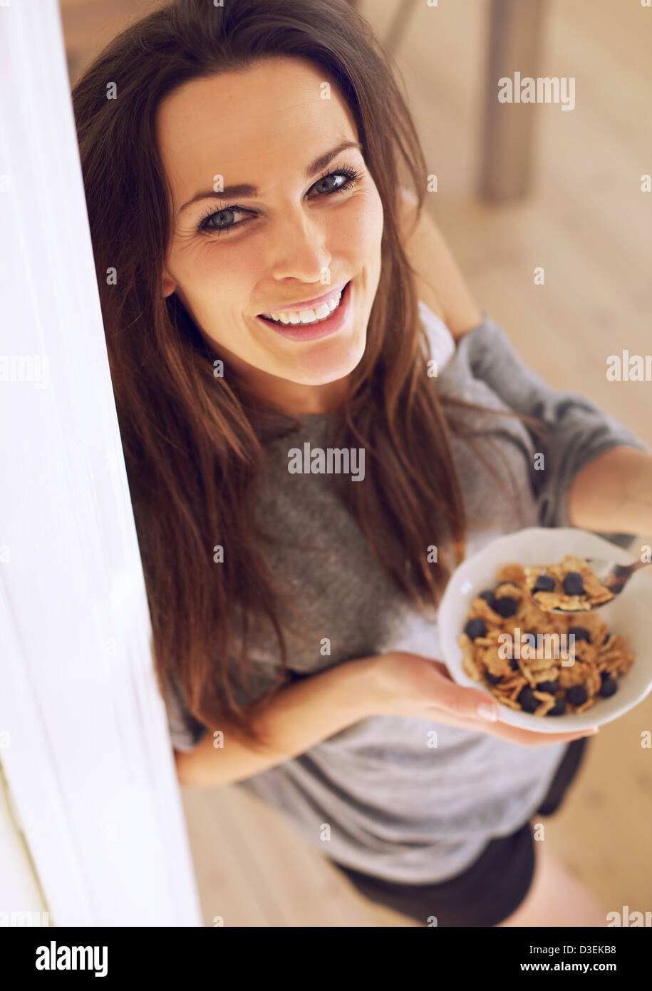 Charming woman looking up while eating her breakfast standing up Stock