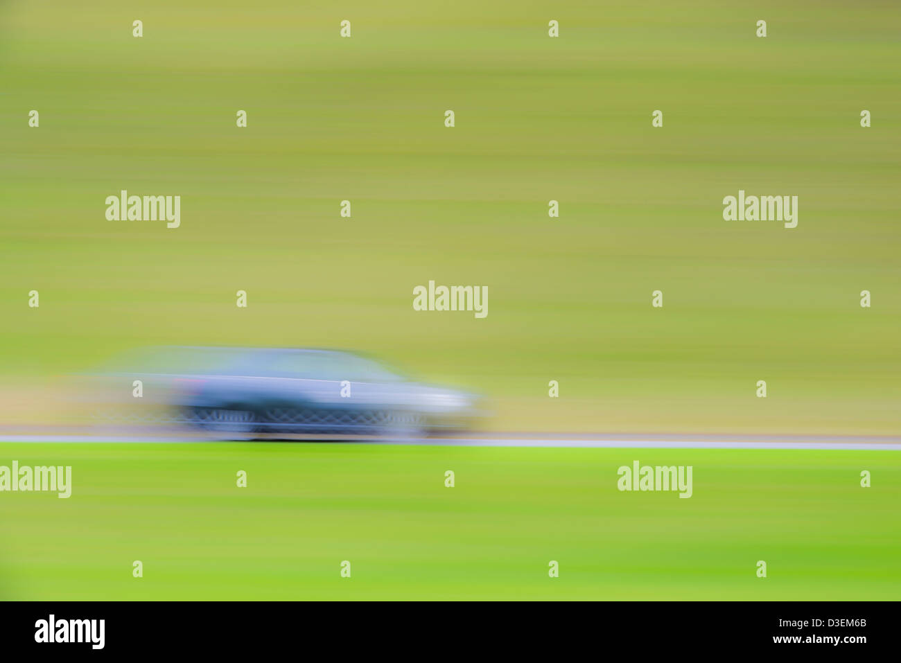 Blurred motion of one car travelling on road in green landscape Stock Photo