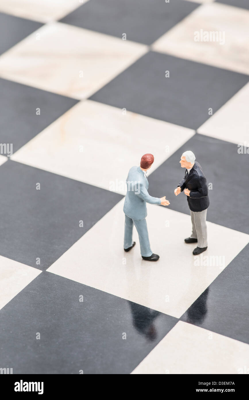 Two small figurines of businessmen standing on chessboard shaking hands Stock Photo