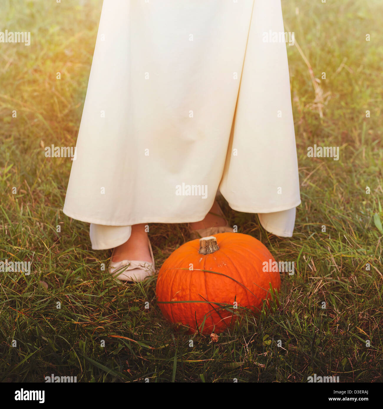 a pumpkin in the grass in front of a woman in a white dress Stock Photo