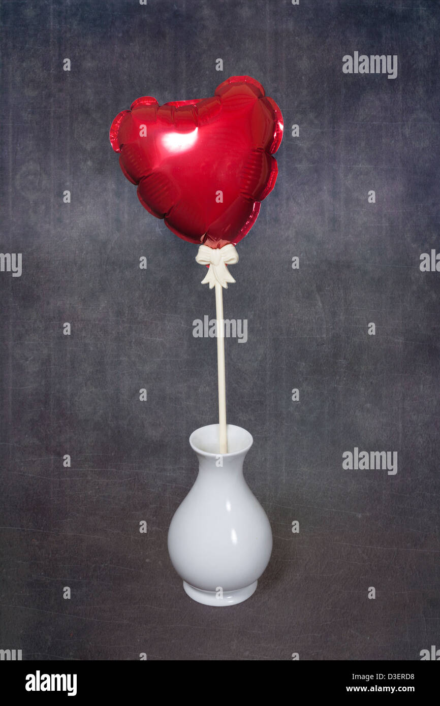 a red, heart-shaped balloon in a white vase Stock Photo