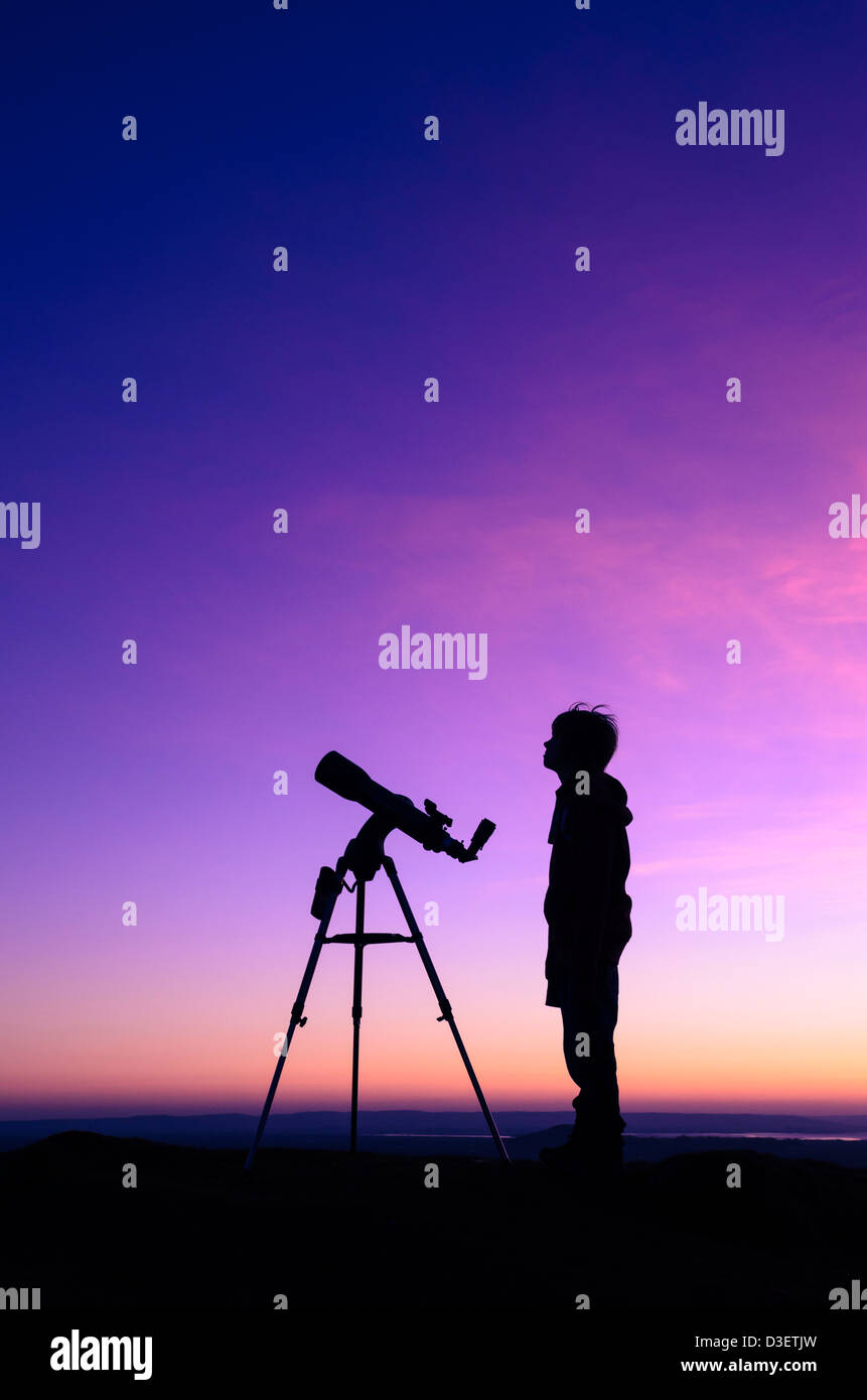 The silhouette of a teenage boy stargazing with a telescope at dusk Stock Photo
