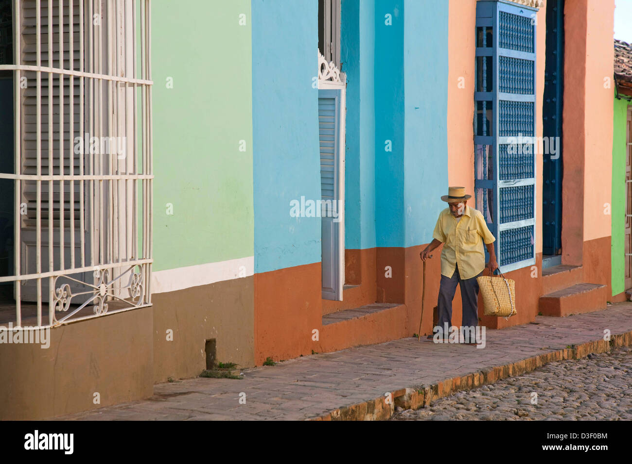 Old Cuban man walking along pastel coloured houses with barrotes and grilles in Trinidad, Cuba Stock Photo