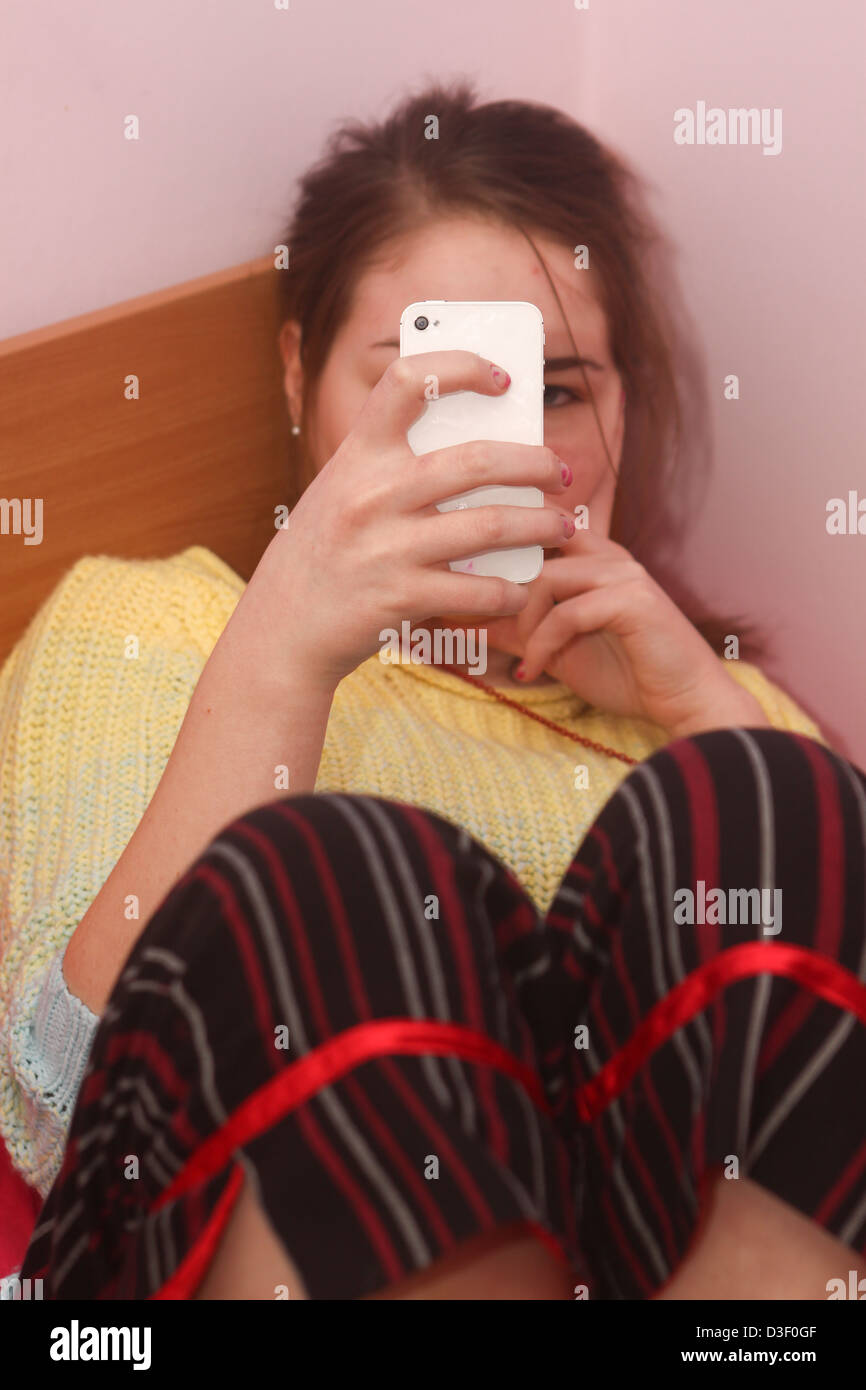 Teenage girl sitting on bed texting on iPhone Stock Photo