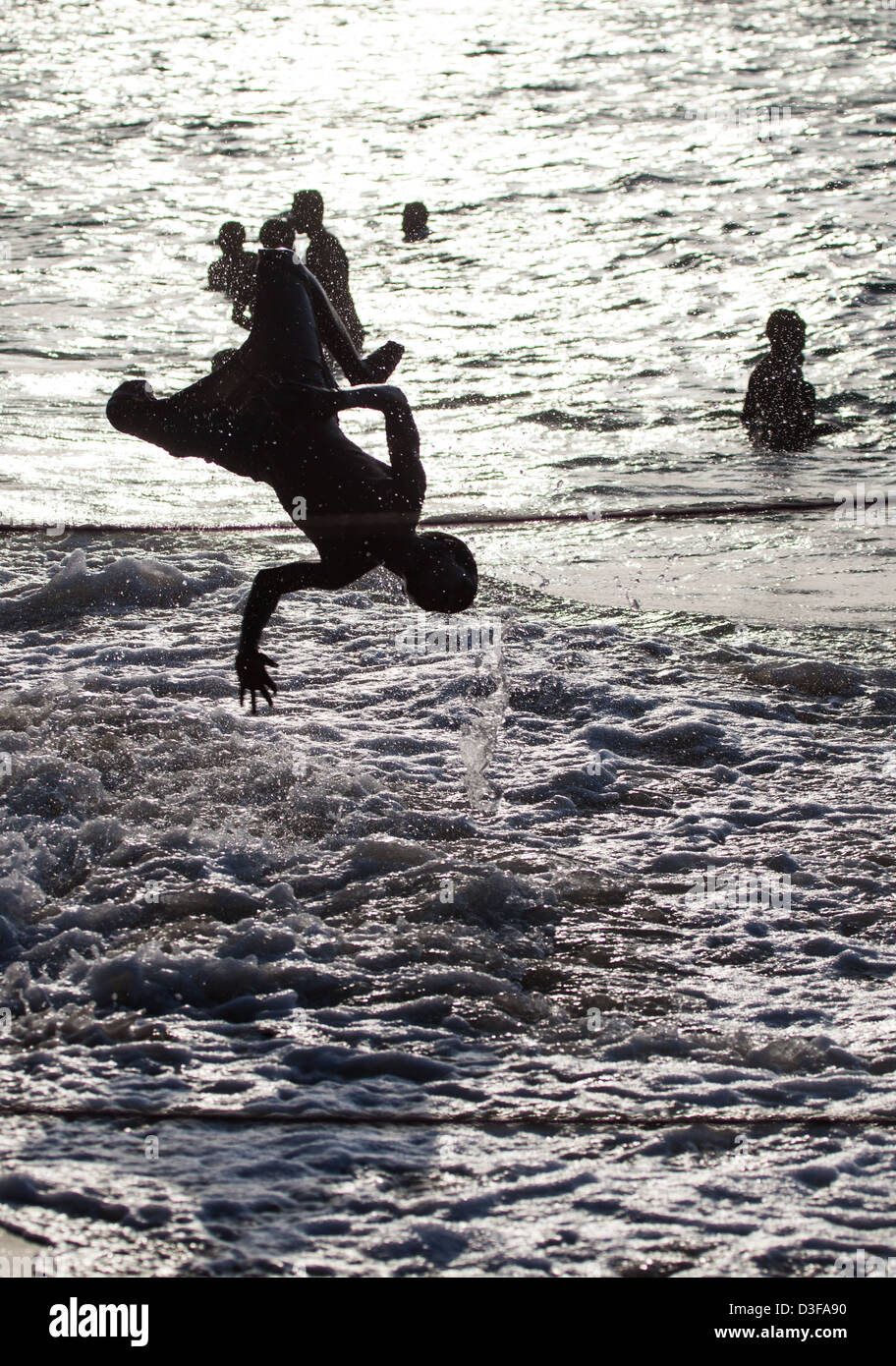 A teenager does a flip into the surf as the sun sets behind him. Zanzibar, Tanzania Stock Photo