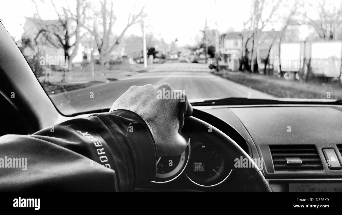 First person view of man driving car with steering wheel and hand. Black and white. Stock Photo