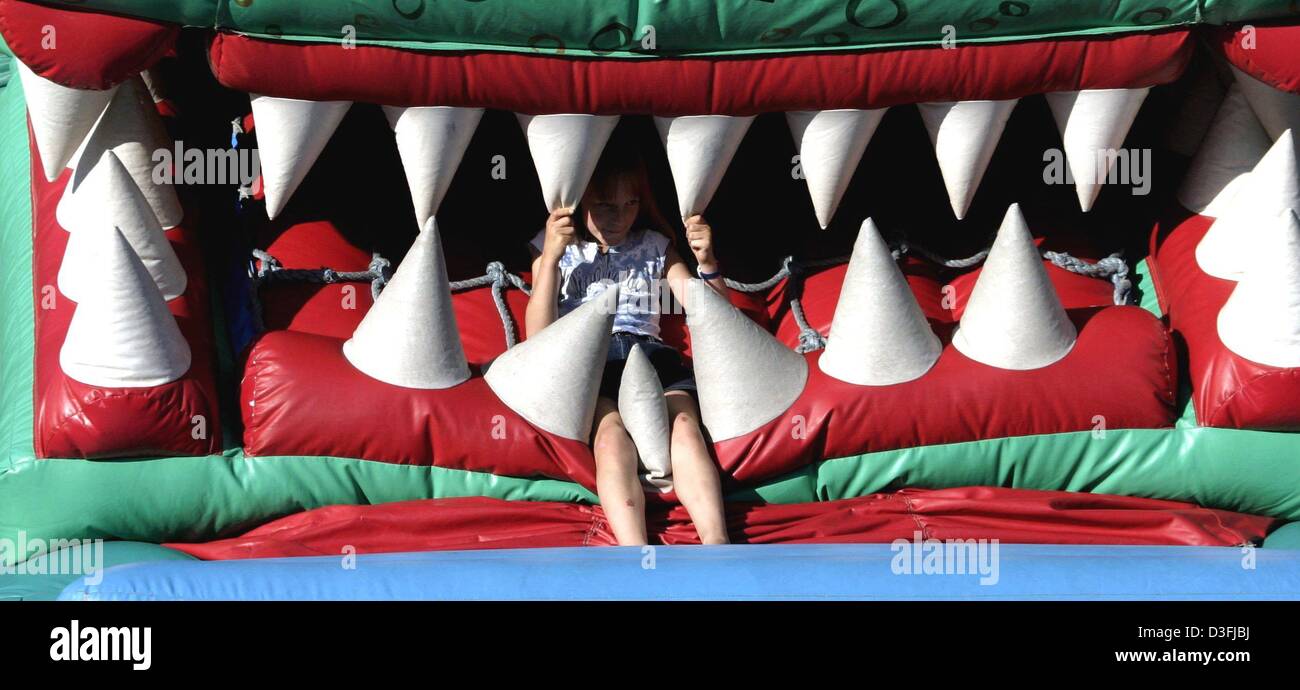 (dpa) - A child is sitting between the teeth of a huge dragon which is in fact a bouncy castle, Muelheim, Germany, 10 July 2003. Stock Photo