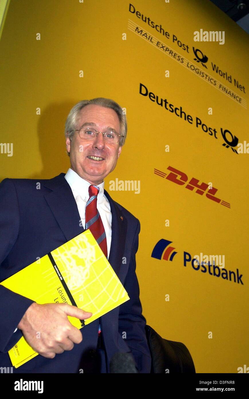 (dpa) - Klaus Zumwinkel, CEO of the Deutsche Post AG, smiles in front of the logos of the companies belonging to the Deutsche Post AG group, in Bonn, Germany, 25 March 2003. The German Post is to close 700 post offices by the end of 2004, and will continue to cut jobs over the next years. Vacancies are not going to be filled in the future, which will amount to several thousand jobs Stock Photo