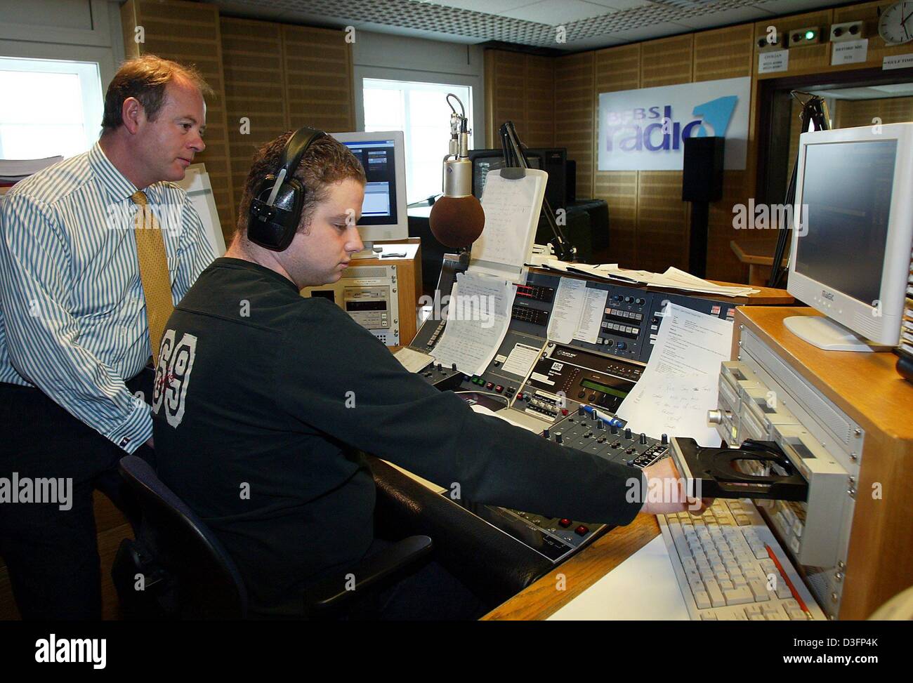 dpa) - Patrick Eade (L), General Manager of the British radio station BFBS-Radio  1, looks over the shoulder of radio dj and presenter James Macdonald in the  recording studio of BFBS-Radio1. The