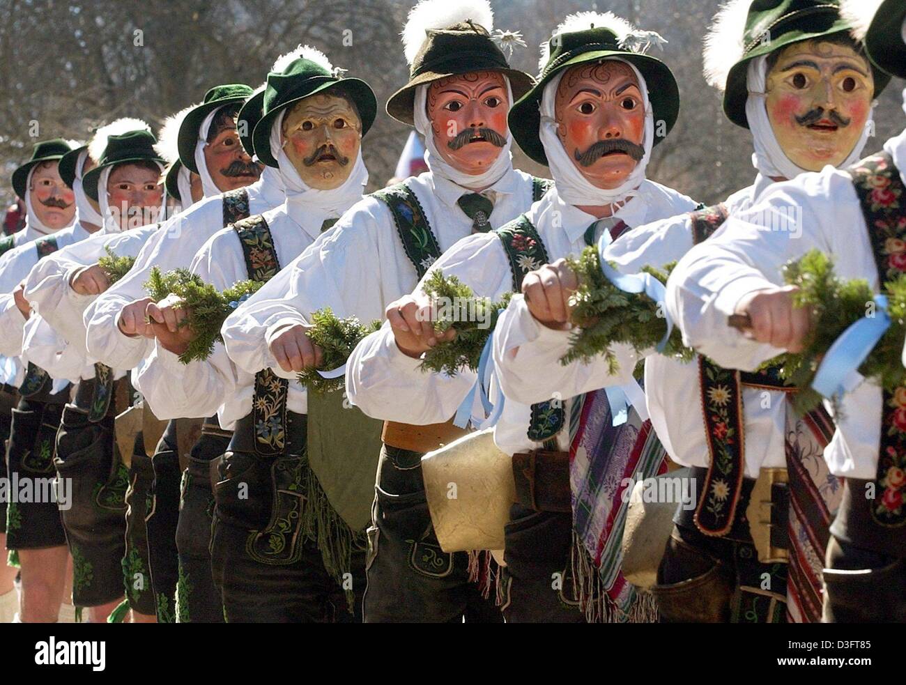 (dpa) - Masked men clad in identical Bavarian lederhosen (leather shorts) parade along a street while ringing cow bells in Mittenwald, Bavaria, Germany, 27 February 2003. As a carnival tradition, these 'bell stirrers' ('Schellenruehrer') and their noise are meant to scare off the mean winter demons. Stock Photo