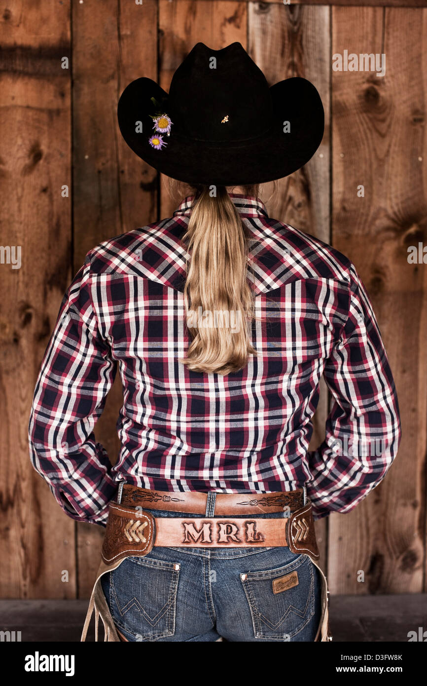 Cowgirl wrangler standing with checked shirt, rear view, Montana, USA Stock Photo