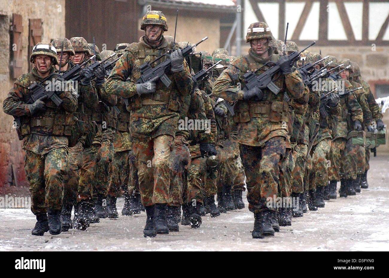 (dpa) - A platoon of the Infantry School of the German Bundeswehr marches through the uninhabited village 'Bonnland' in Hammelburg, Germany, 3 February 2003. 'Bonnland' is a village of vacated and empty buildings used as scenery for military drills. The 100-year-old houses have no window panes and no furniture, which makes them an ideal site for the training of how to conquer villa Stock Photo