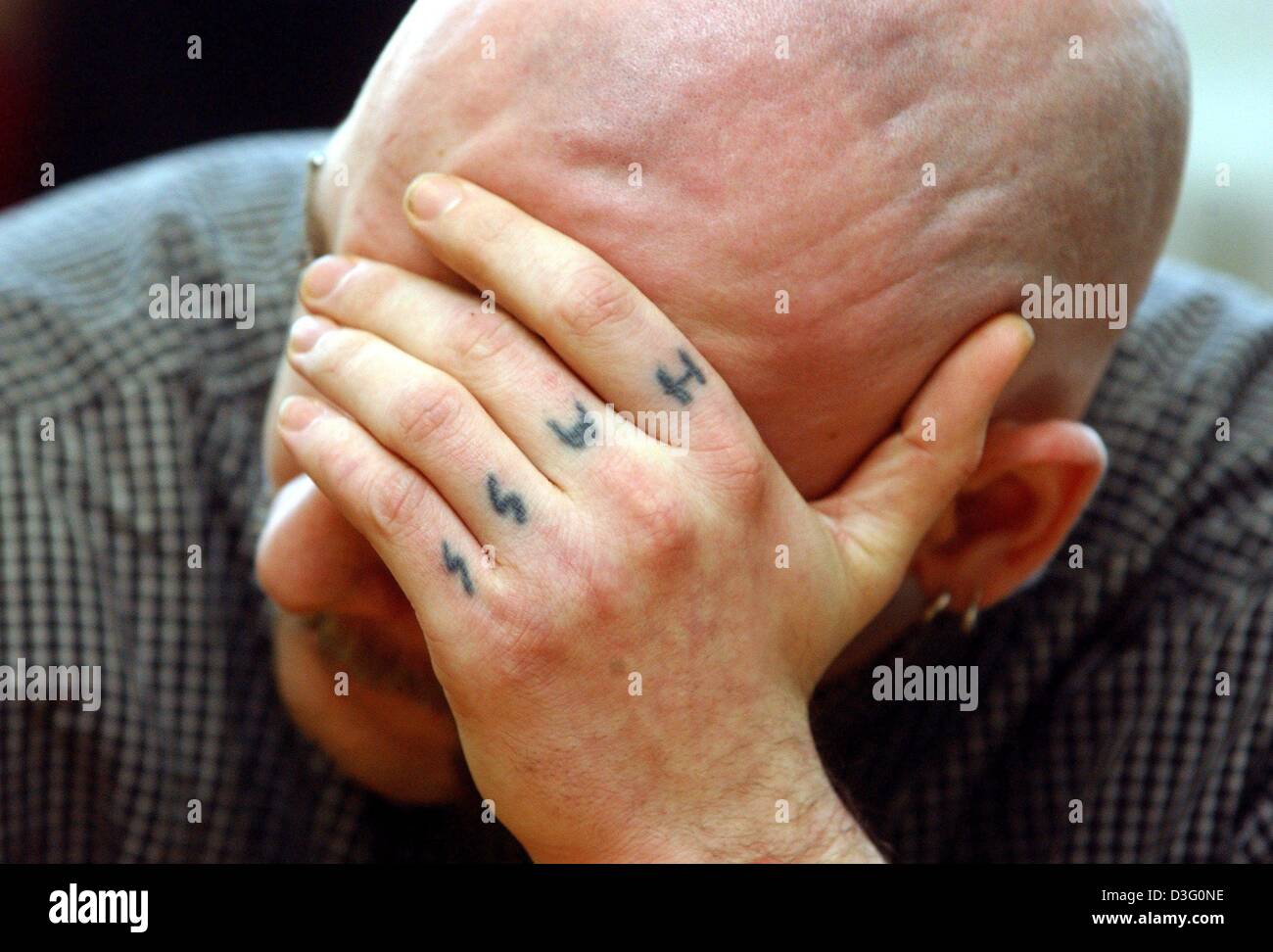 (dpa) - Defendant Matthias R. covers his face with his hand, which bears the tattoo 'Hass' ('hate') on four of his fingers, during his trial for the suspected murder of a 29-year-old at the District Court in Frankfurt Oder, eastern Germany, 11 February 2003.  The tattoo is commonly found among those involved in the Neo-Nazi scene.  The 23-year-old murder suspect is being tried alon Stock Photo