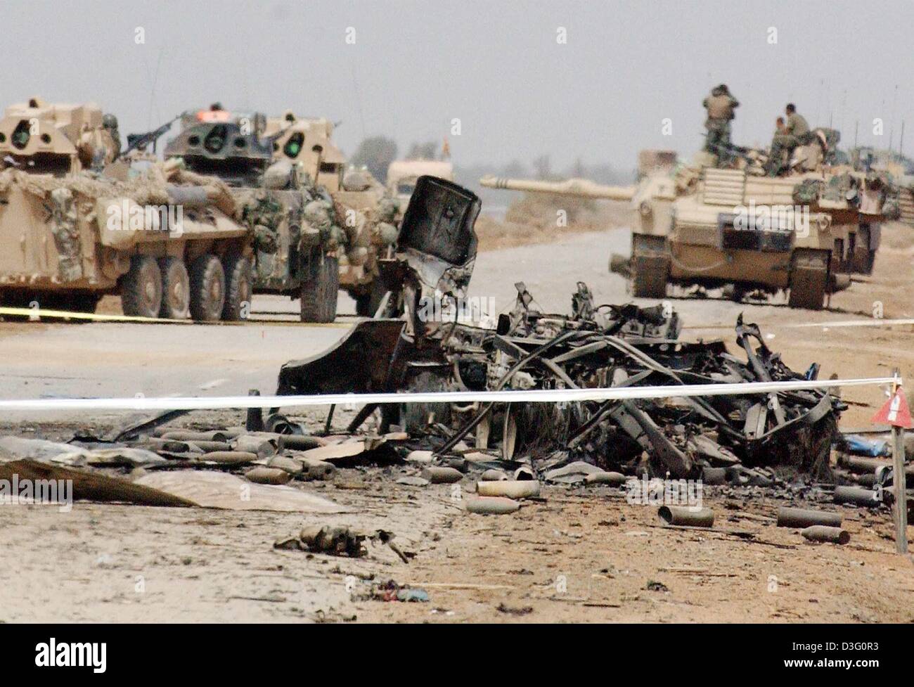 (dpa) - A column of US Marines drive in their vehicles past burnt out and destroyed trucks along the road near Al Aziziyan 40 kilometers south of Baghdad, Iraq, 4 April 2003. US Marines are moving towards the Iraqi capital. The spearheads of US troops are only a few kilometers away from the outskirts of Baghdad. Stock Photo