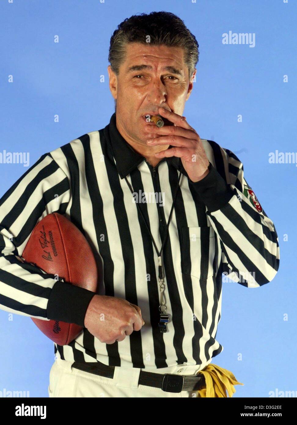 (dpa) - Rudi Assauer, manager of the German soccer club Schalke 04, poses in an American football referee's tricot while smoking a cigar and holding a football in his arm during a photoshoot for the American football club Rhein Fire in a studio in Mettmann, Germany, 12 March 2003. The American football club Rhein Fire will play its home games on the home pitch of the Schalke 04 soc Stock Photo