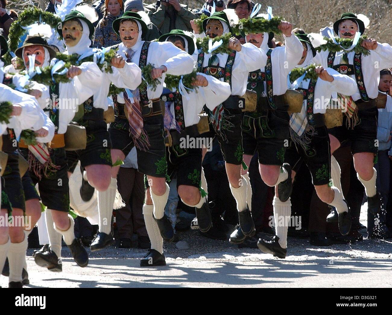 (dpa) - Masked men clad in identical Bavarian lederhosen (leather shorts) parade along a street while ringing cow bells in Mittenwald, Bavaria, Germany, 27 February 2003. As a carnival tradition in Mittenwald, these 'bell stirrers' ('Schellenruehrer') and their noise are meant to scare off the mean winter demons. Stock Photo