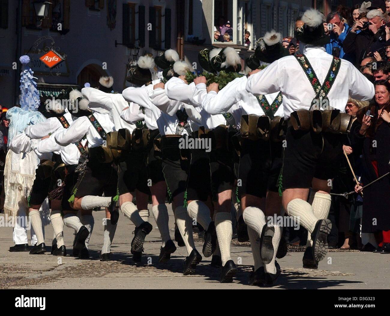 (dpa) - Masked men clad in identical Bavarian lederhosen (leather shorts) parade along a street while ringing cow bells in Mittenwald, Bavaria, Germany, 27 February 2003. As a carnival tradition, these 'bell stirrers' ('Schellenruehrer') and their noise are meant to scare off the mean winter demons. Stock Photo