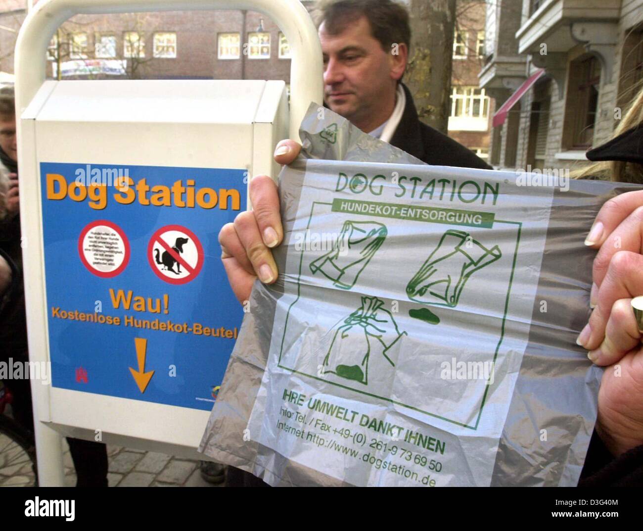 (dpa) - A person holds up a plastic bag next to a 'dog station' in Hamburg, northern Germany, 12 February 2003.  The plastic bags even have a diagram printed on them explaining their use.  The sign on the dog station reads 'Dog Station, Wau!, Kostenlose Hundekot-Beutel' ('Dog Station, Woof woof!, Free dog feces bags').  In the future, dog owners are supposed to use these bags to re Stock Photo