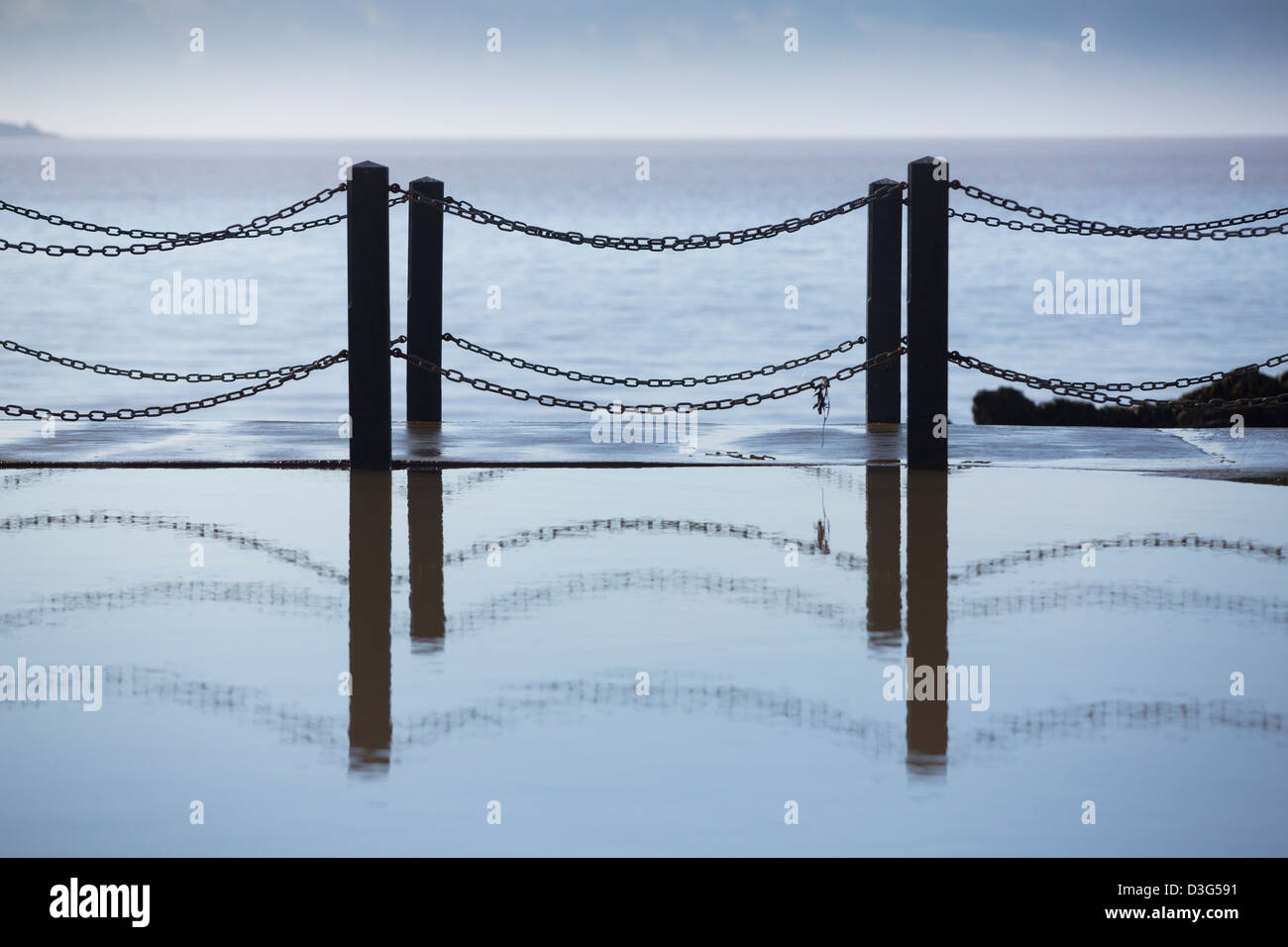 Fence reflected in a pool of water with the sea in the background Stock