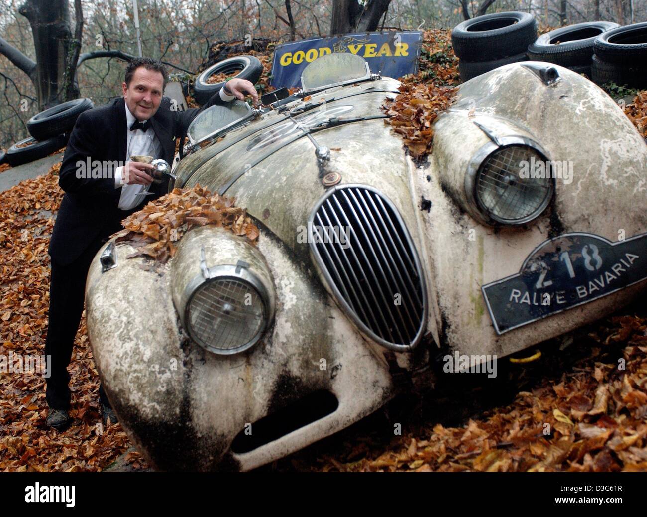 (dpa) - Michael Froehlich holds a glass of white wine while he leans onto a Jaguar XK 120 from the year 1950, which is in the process of decomposing in his garden near Mettmann, Germany, 16 November 2003. Froehlich, who was born in 1950, had bought 50 historic cars of the year 1950 on his 50th birthday three years ago. Since, the rotting cars are left outside and form a gallery of  Stock Photo